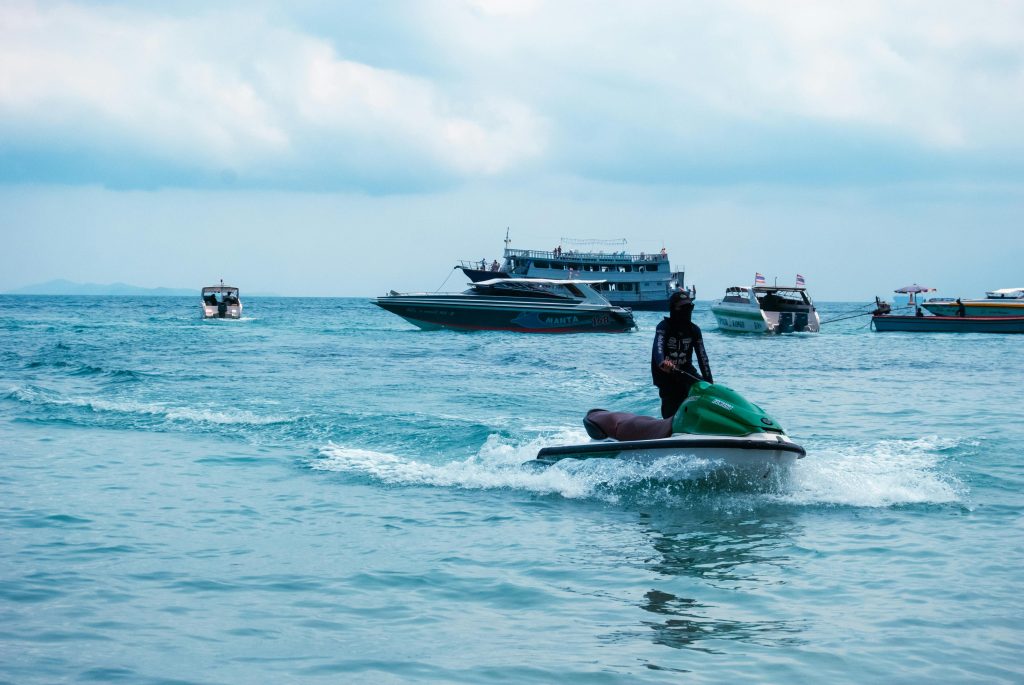 A lone rider enjoying a thrilling jet ski ride amidst boats on a sunny blue ocean.