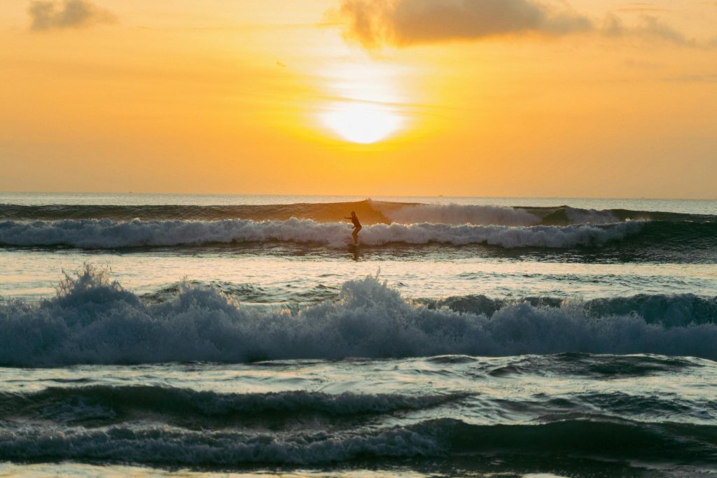 A surfer rides the waves during a vibrant sunset on a Bali beach, capturing a stunning tropical scene.